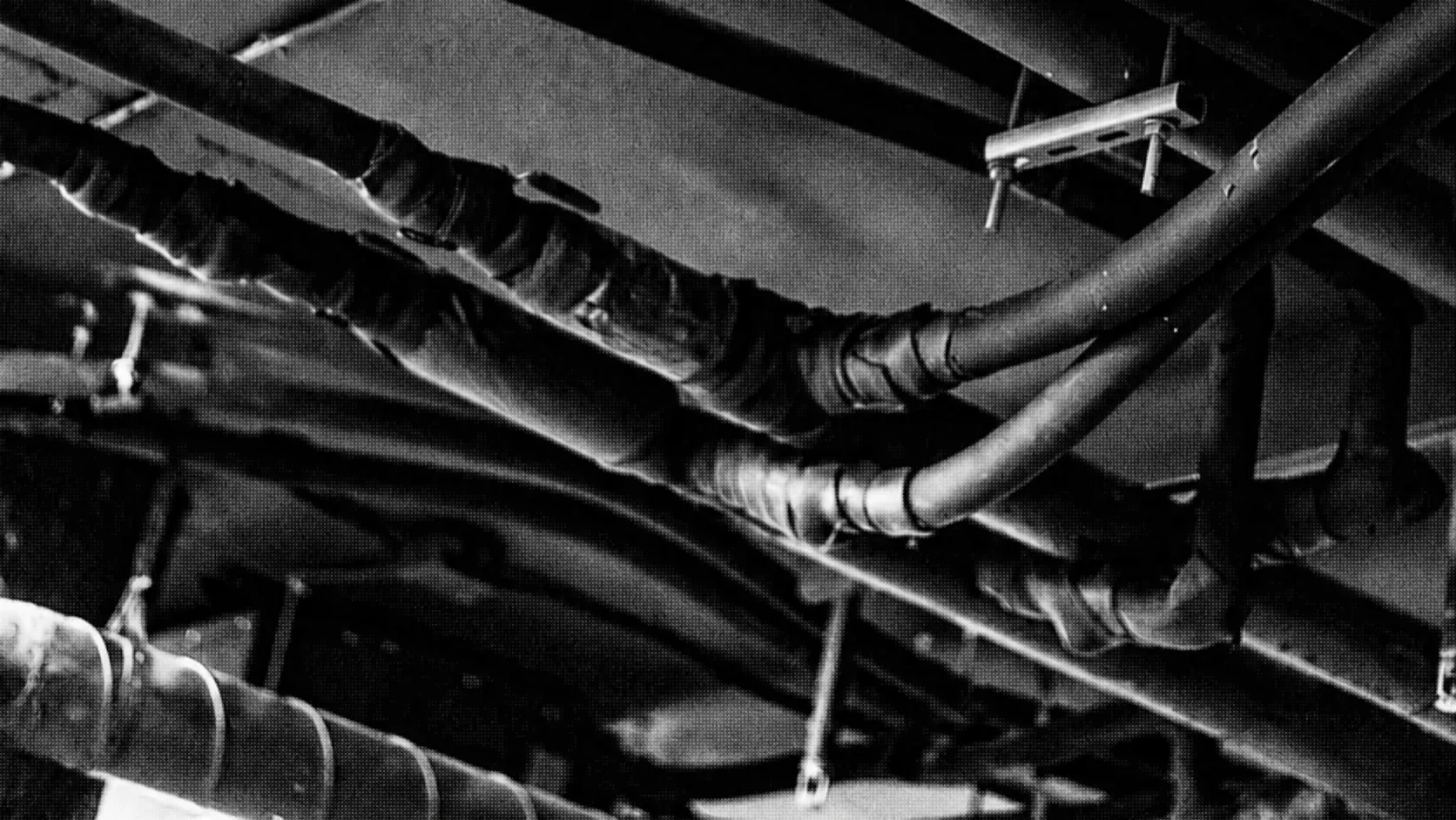 Dense network of industrial pipes crossing a dark ceiling