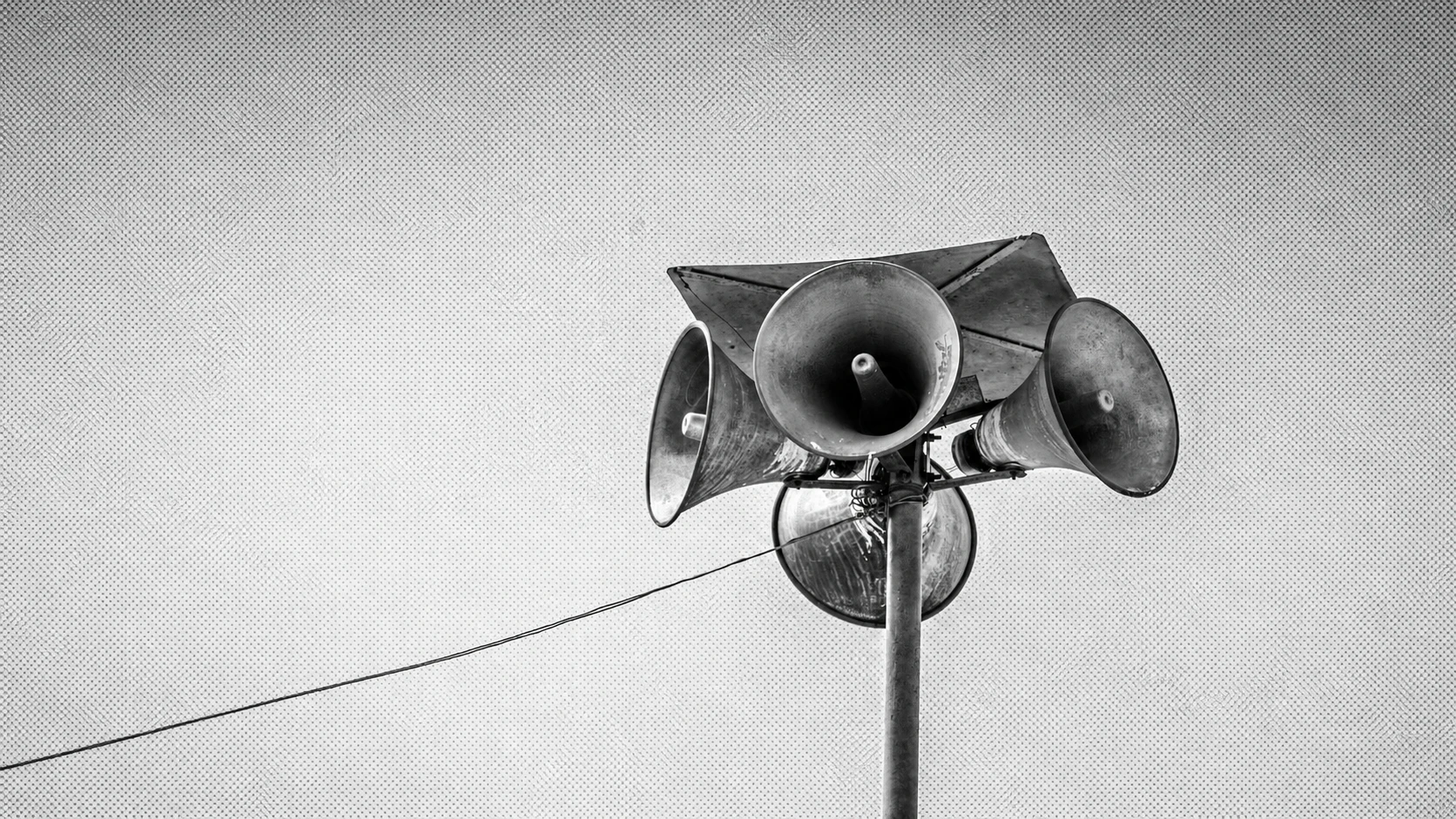 Cluster of outdoor loudspeakers mounted on a pole against an empty sky