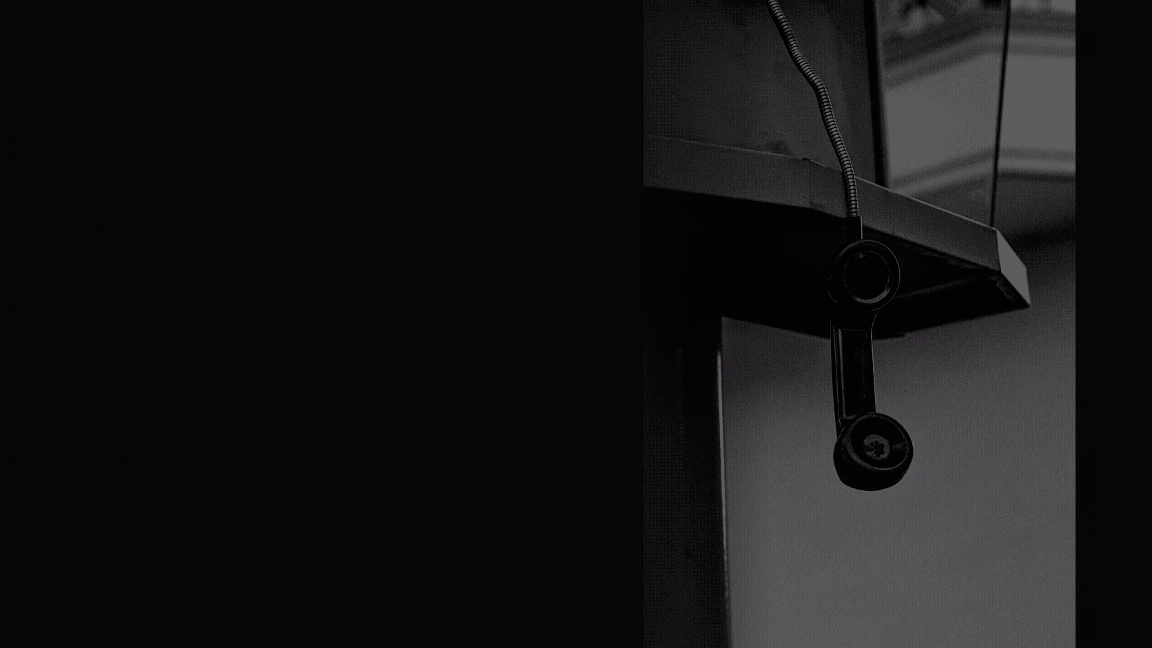 A vintage black telephone receiver hanging from its cord with no one nearby
