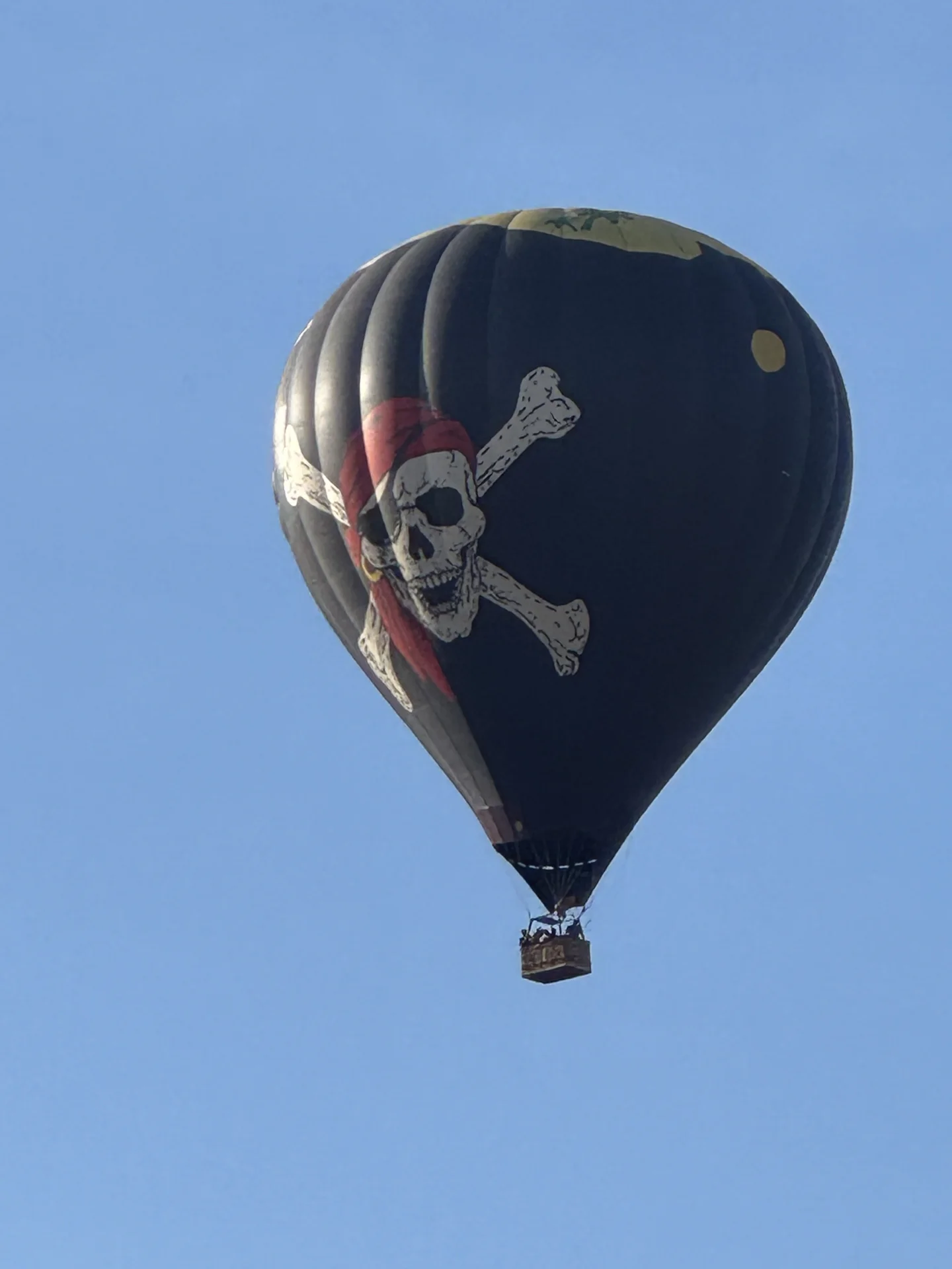 Black hot air balloon with a skull and crossbones against a clear blue sky