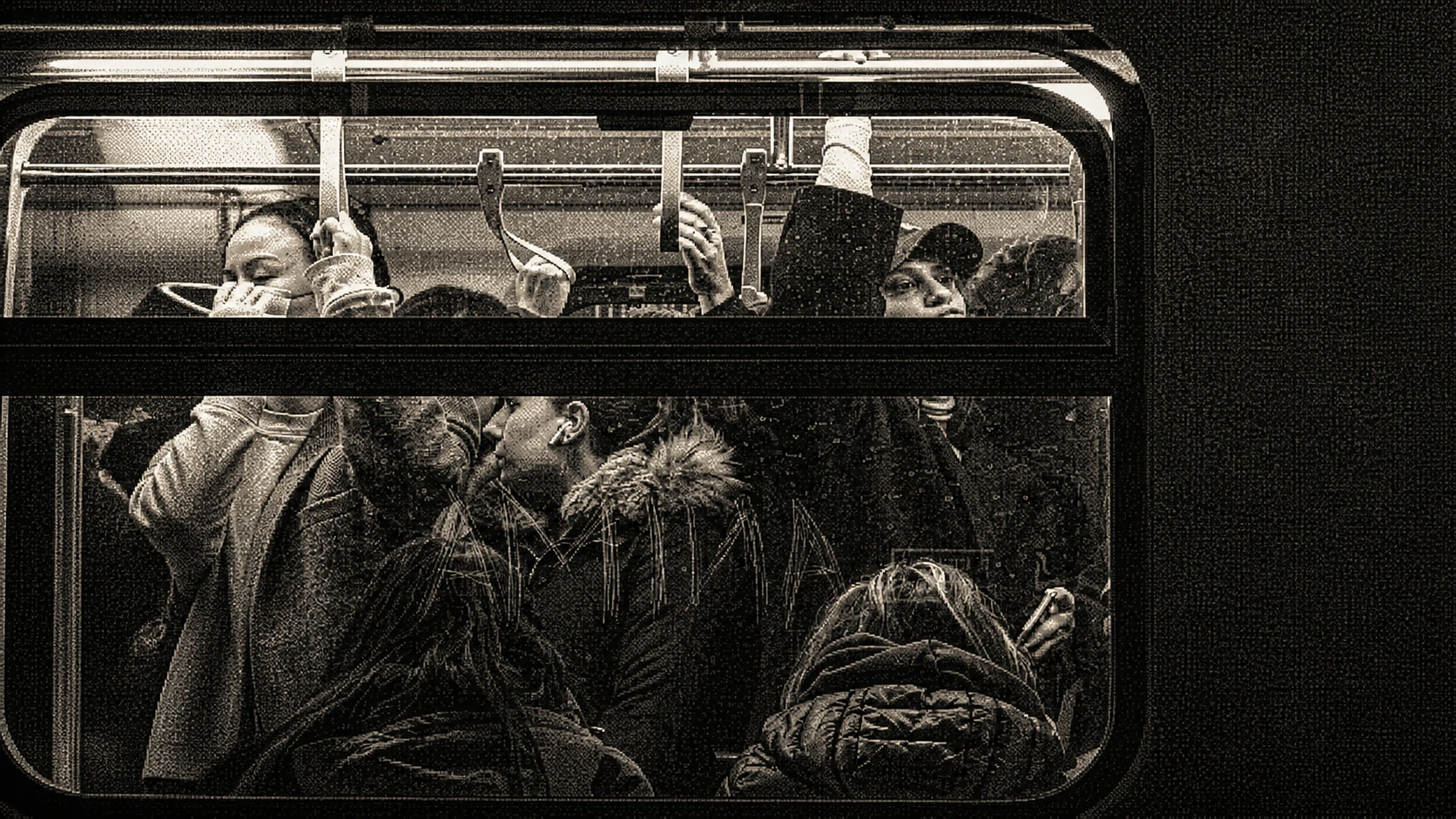 Crowded train car seen through its windows, with passengers holding straps and looking in different directions